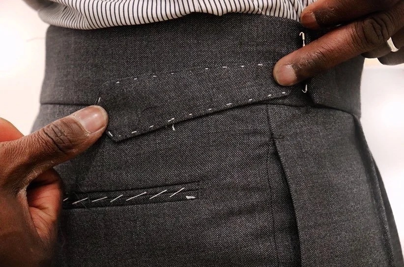 Chemise prototype en denim suspendue à un miroir ancien dans l’atelier, devant les liasses de tissus