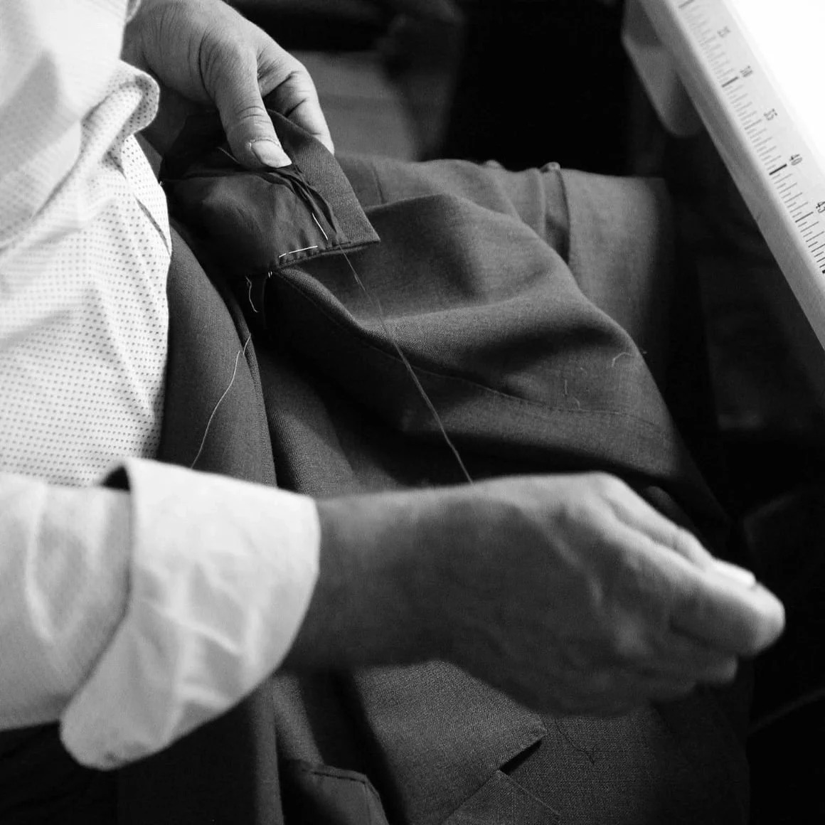 Mains du tailleur cousant une épaule de veste au fil, point par point