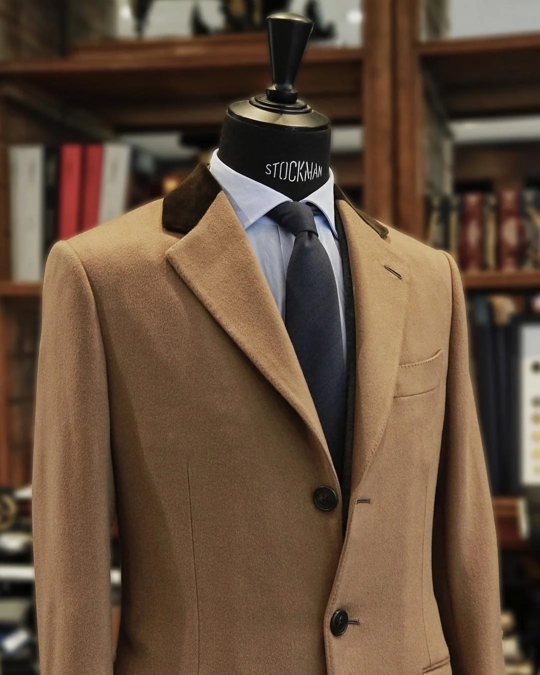 Manteau en poil de chameau à col de velours présenté sur mannequin devant la bibliothèque de tissus