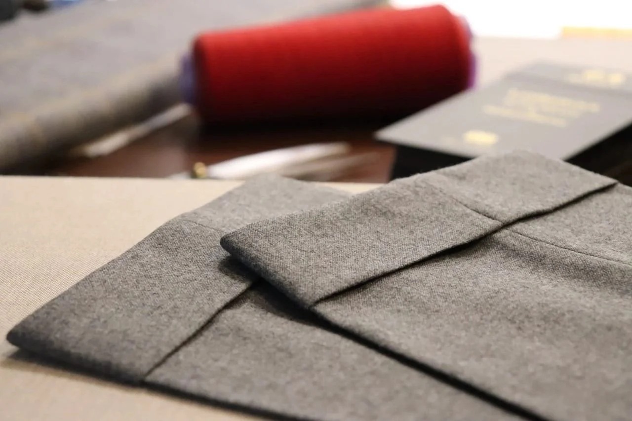 Pantalons pliés sur la table de l’atelier, bobine de fil posée en arrière-plan