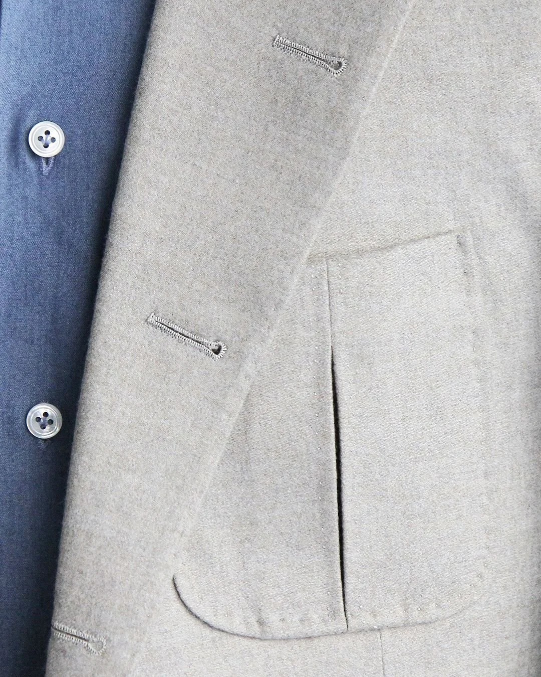 Détail des boutonnières cousues main d’une veste en flanelle écrue portée sur une chemise bleue
