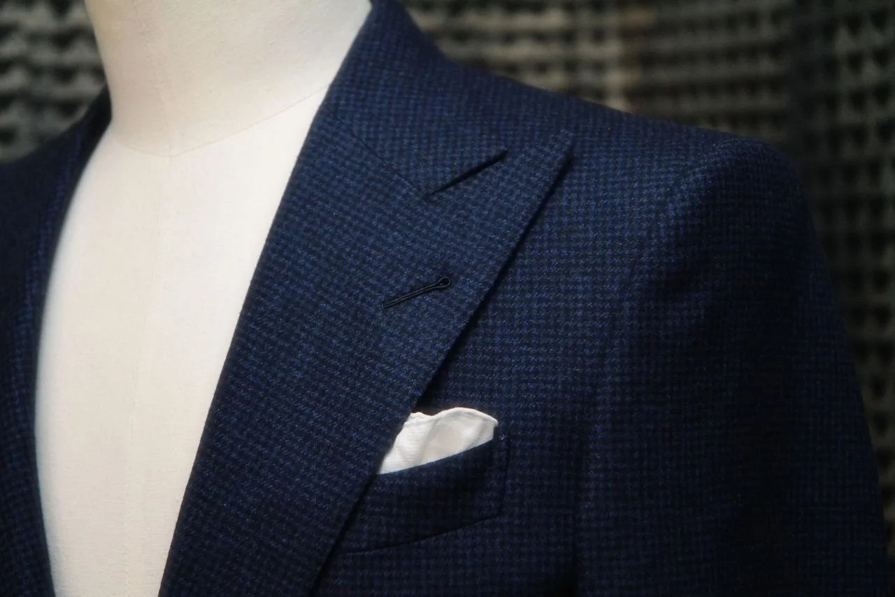Détail du revers d’une veste pied-de-poule bleu nuit avec pochette blanche